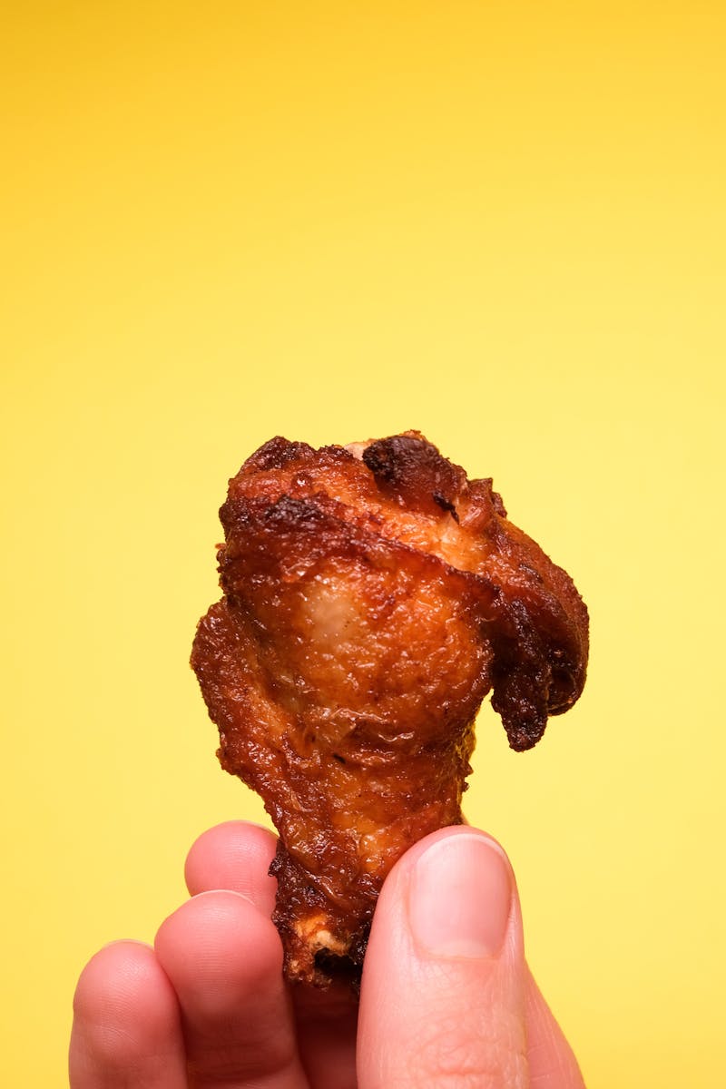 Crop faceless person with tasty fried chicken in hands on yellow background in light studio