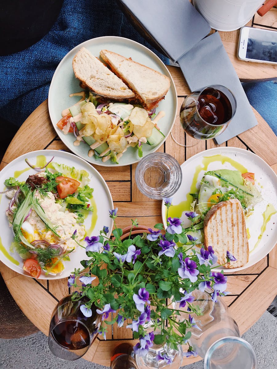 Overhead view of a tasty lunch with sandwiches, salads, and wine on a wooden table, perfect for a delightful meal experience.