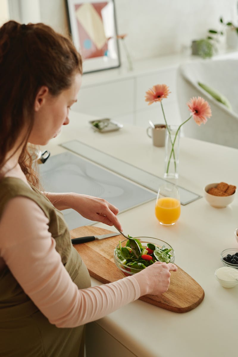 A pregnant woman prepares a nutritious vegetable salad in a bright kitchen setting.